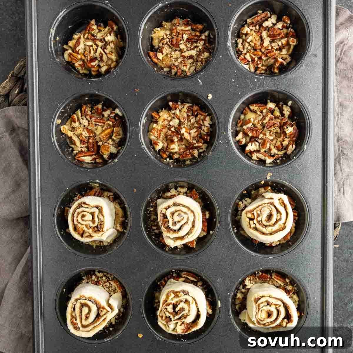 A muffin tin with six cups filled with chopped nuts and six cups with unbaked puff pastry sticky buns, ready for baking.