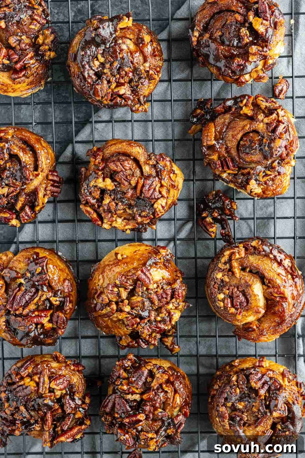 Twelve easy sticky buns cooling on a wire rack, each topped with a glossy caramelized pecan mixture.