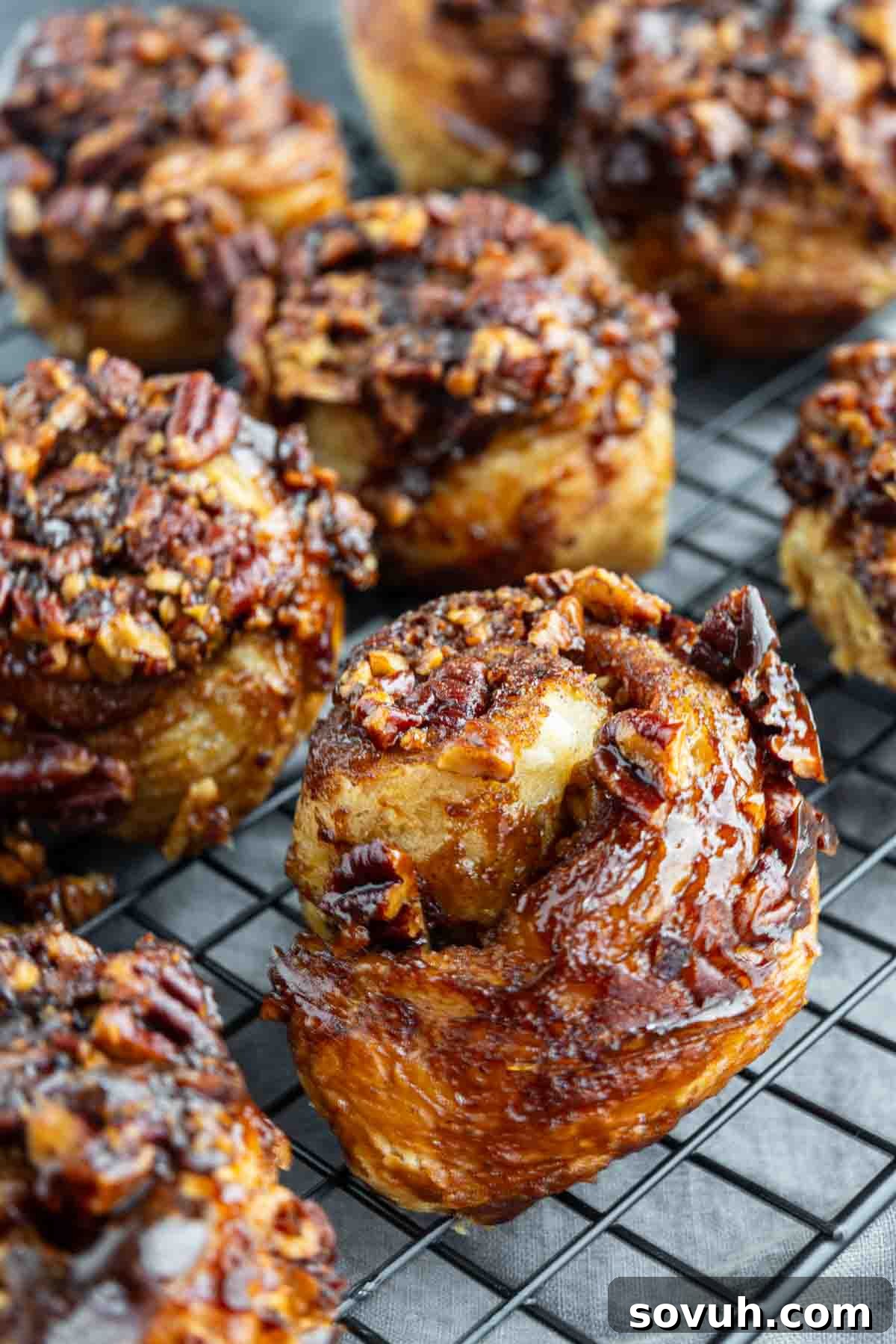 Sticky buns with pecans cooling on a wire rack, topped with caramelized pecans and a glossy glaze.