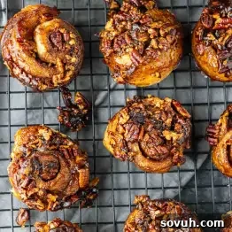 Pecan sticky buns cooling on a wire rack, topped with caramelized pecans and glaze.