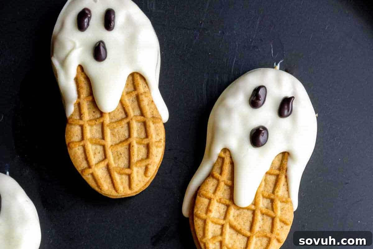 Two cookies shaped like ghosts with white icing and chocolate eyes on a black background.