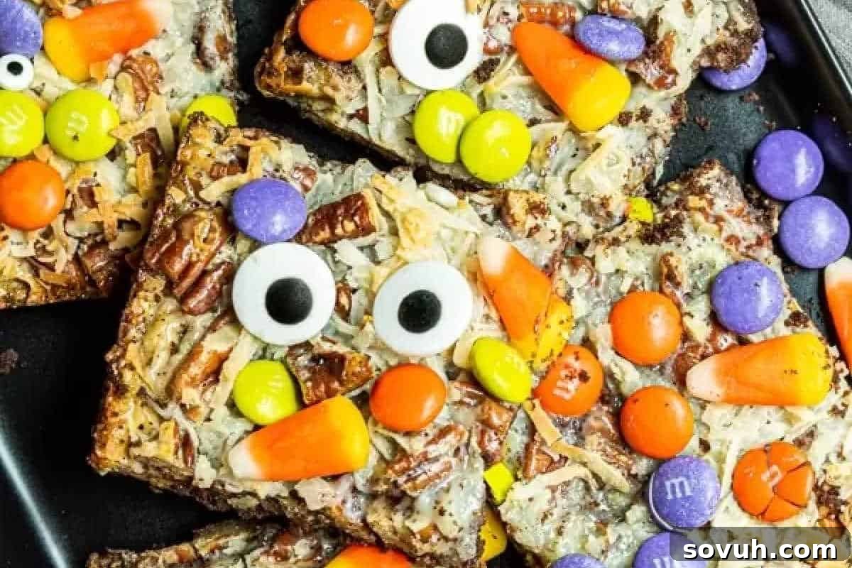 Colorful Halloween-themed treats topped with candy eyes, candy corn, M&M's, pretzels, and coconut on a baking tray.