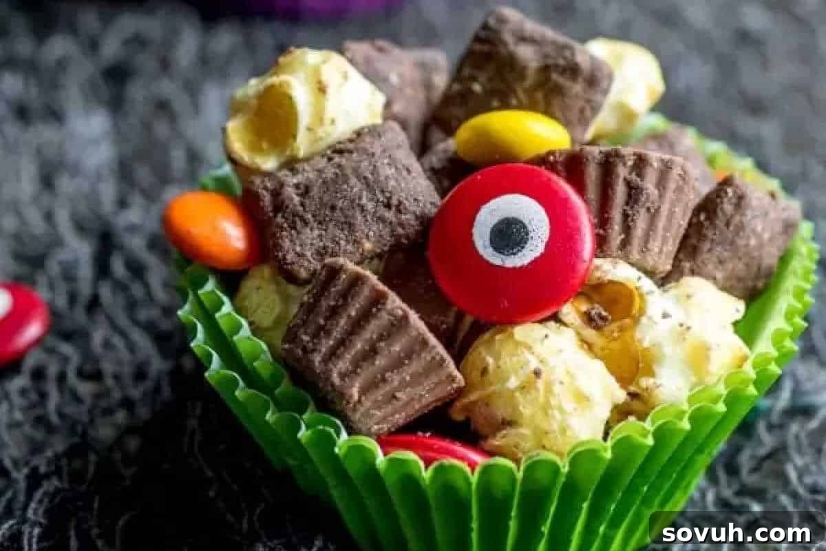 A green cupcake liner holds a snack mix of chocolate pieces, popcorn, and colorful candy, including one with an eye design.