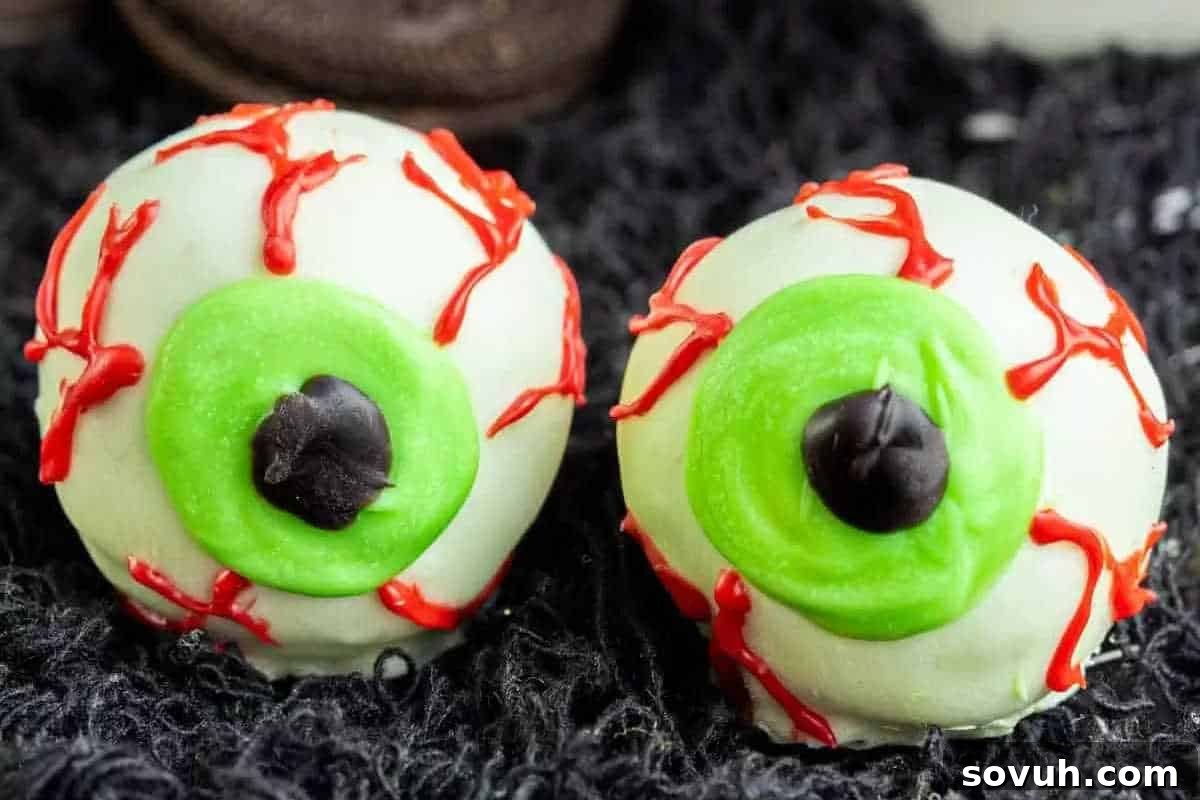 Two eyeball-shaped treats with green irises and red frosting veins, set on a dark textured surface.