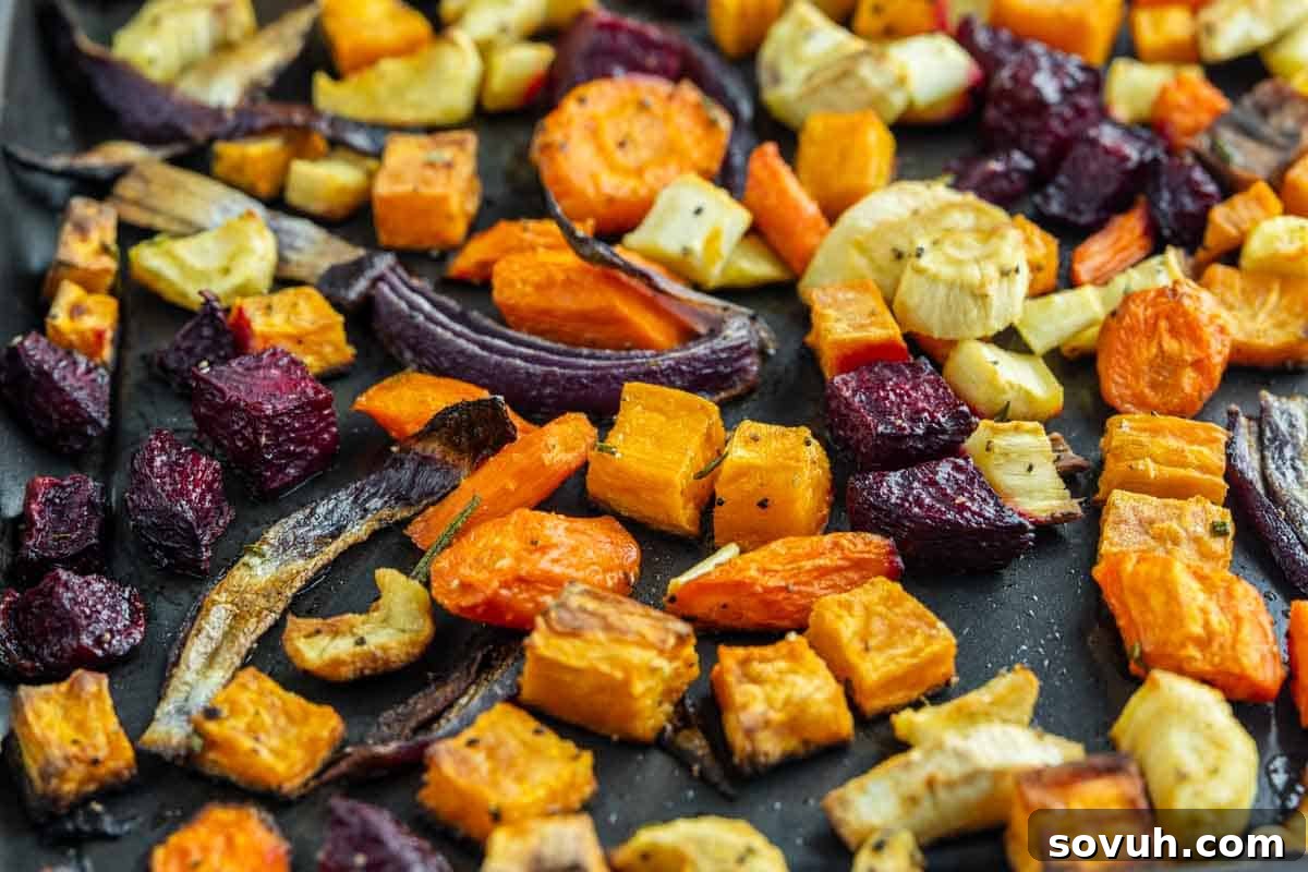 A baking tray filled with roasted root vegetables—including carrots, beets, onions, parsnips, and sweet potatoes—cut into chunks and lightly browned, ready to be served.