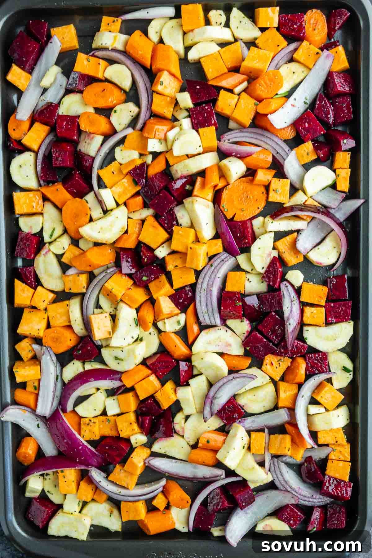 A baking sheet filled with chopped assorted vegetables, including carrots, beets, zucchini, red onion, and sweet potatoes—seasoned and ready for oven roasting.