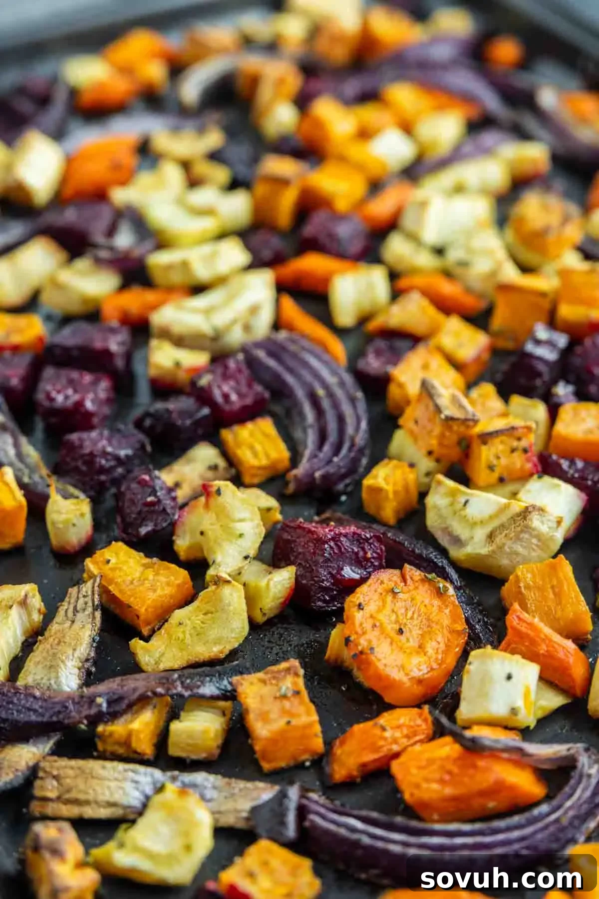 A baking sheet filled with assorted oven roasted vegetables, including carrots, sweet potatoes, beets, parsnips, and red onions cut into chunks, perfect for any meal.
