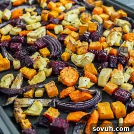 A baking tray filled with assorted roasted vegetables, including carrots, beets, parsnips, sweet potatoes, and red onions, cut into cubes and lightly seasoned.