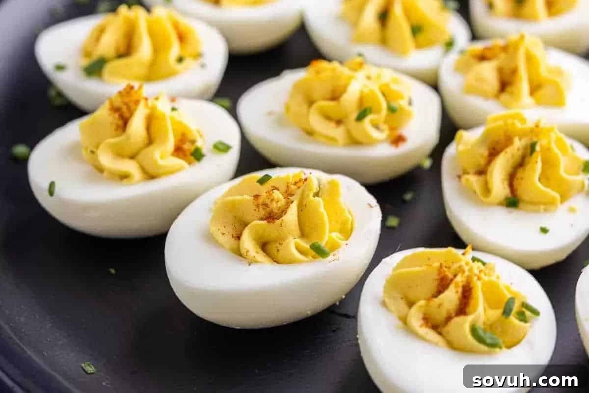 Close-up of deviled eggs topped with paprika and chopped chives on a black surface.