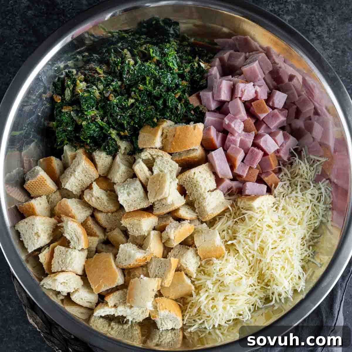 A bowl with ham, cheese, spinach and cubed bread for Ham and Cheese Strata.