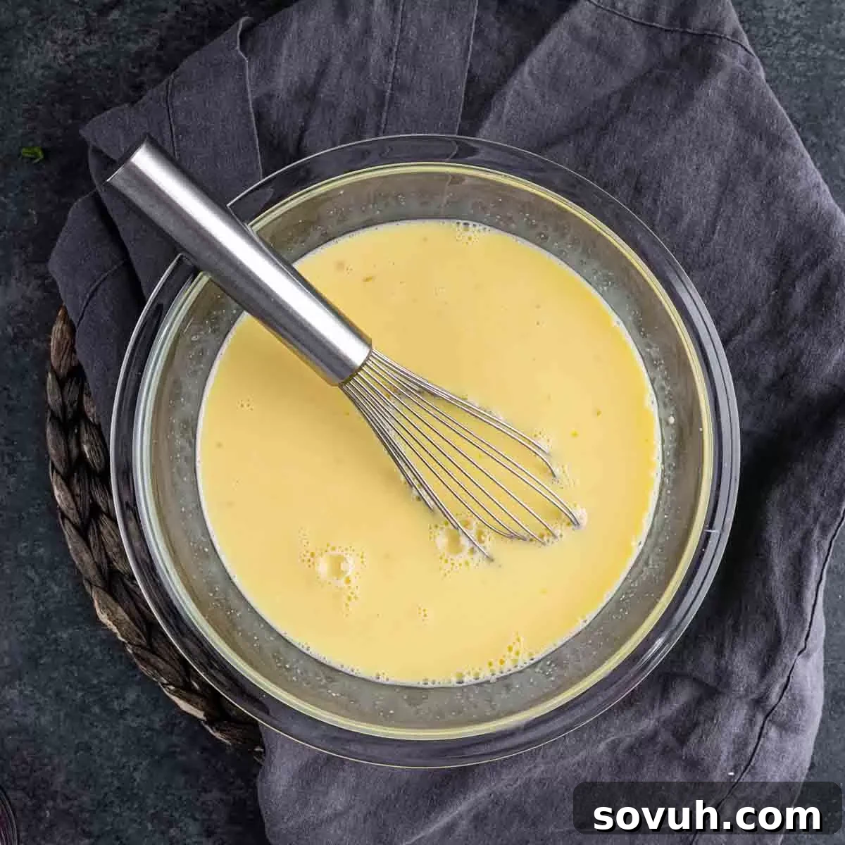 A glass bowl with a whisk in it of egg mixture for Ham and Cheese Strata