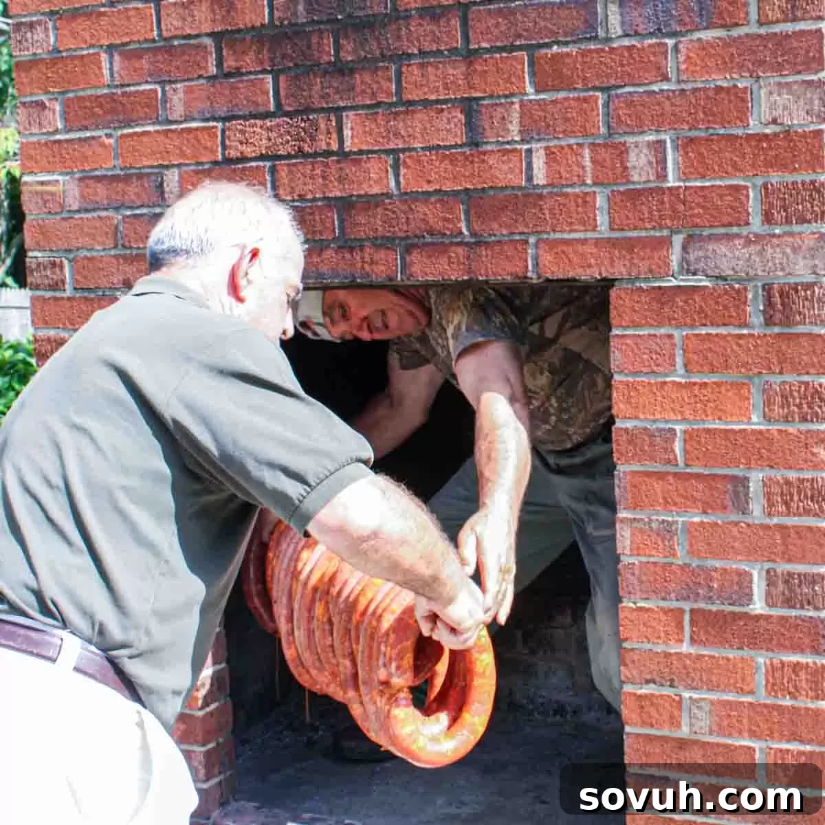Two men carefully placing Portuguese sausage onto racks inside a traditional brick fireplace for smoking