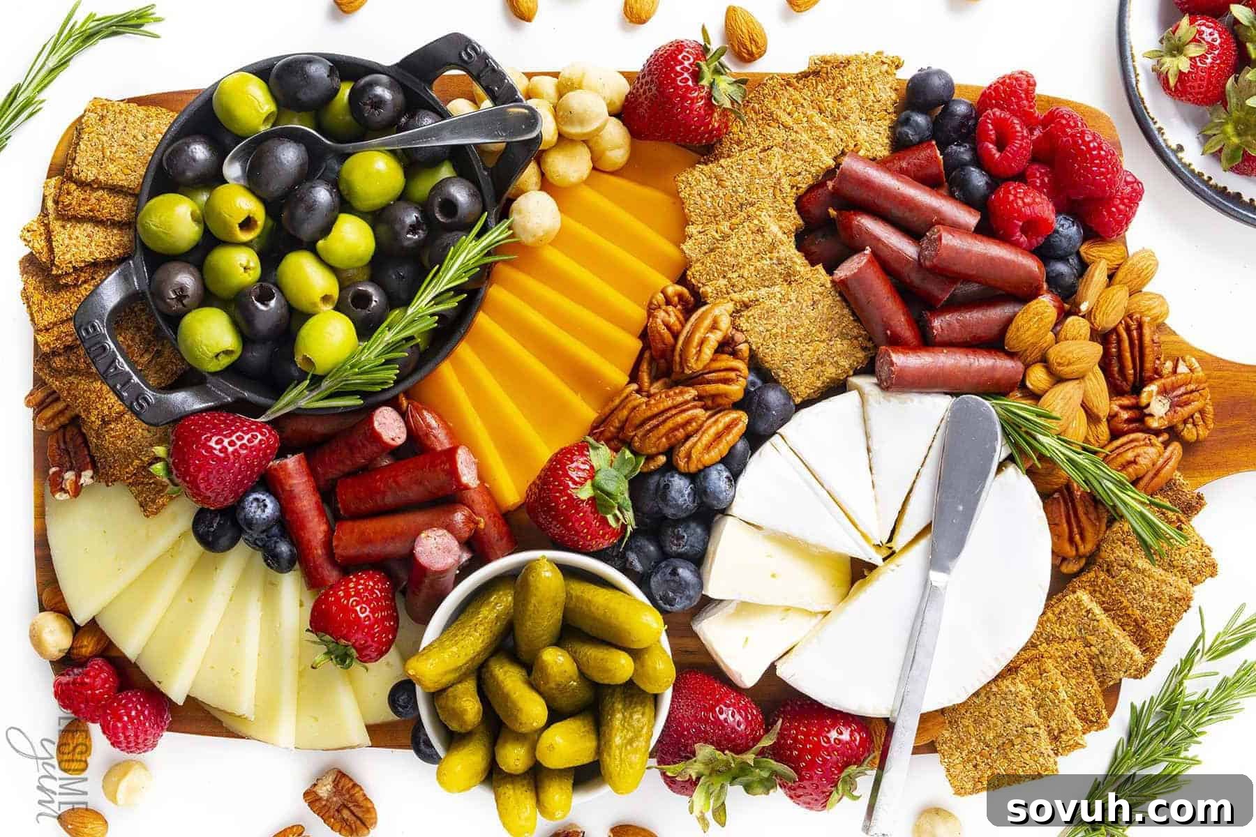 A healthy Keto Charcuterie Board with an enticing array of assorted cheeses, low-carb crackers, cured meats, olives, strawberries, blueberries, pickles, and mixed nuts, garnished with fresh rosemary sprigs.