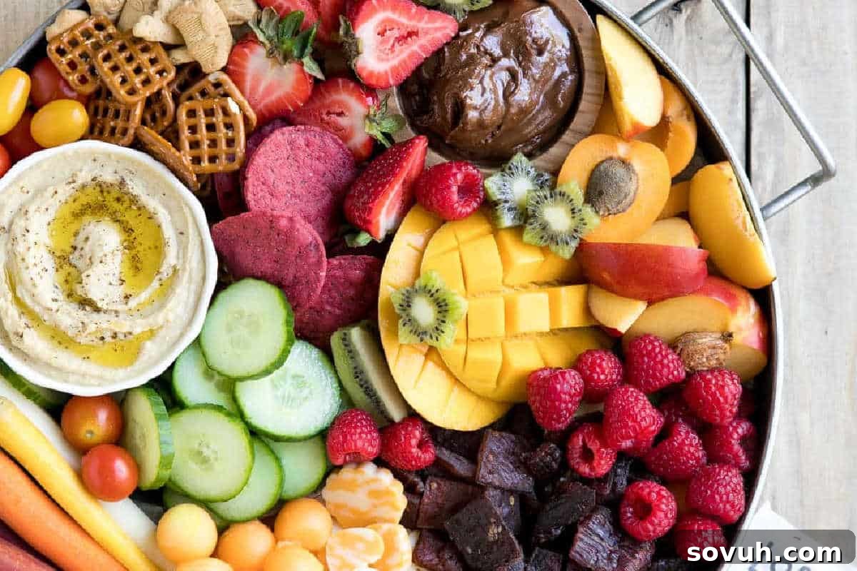 A fun Kid-Friendly Charcuterie Board brimming with an assortment of fresh fruits, sliced vegetables, pretzels, crackers, cheese cubes, creamy hummus, and a sweet chocolate dip.