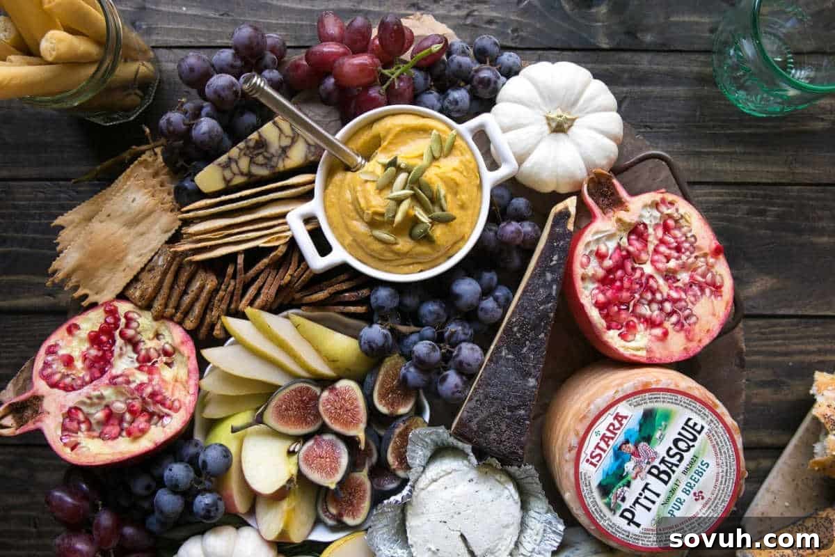A bountiful Autumn Cheese Board (vegetarian) featuring sliced fruits, grapes, figs, crackers, dip, assorted cheeses, pomegranate halves, and a small white pumpkin, on a rustic wooden table.