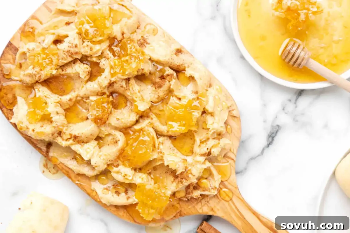 An irresistible Cinnamon Honey Butter Board with torn pieces of crusty bread drizzled with honey, alongside a bowl of honey with a dipper, all beautifully arranged on a wooden serving board.