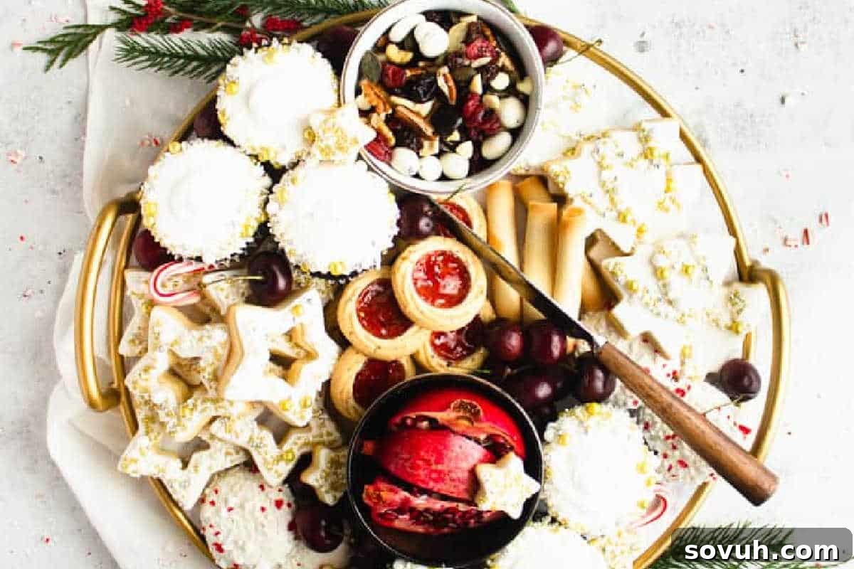 A delightful Cookie Board presented on a gold tray, showcasing an assortment of festive cookies, jam tarts, chocolates, nuts, grapes, and a pomegranate half, adorned with holiday decorations.