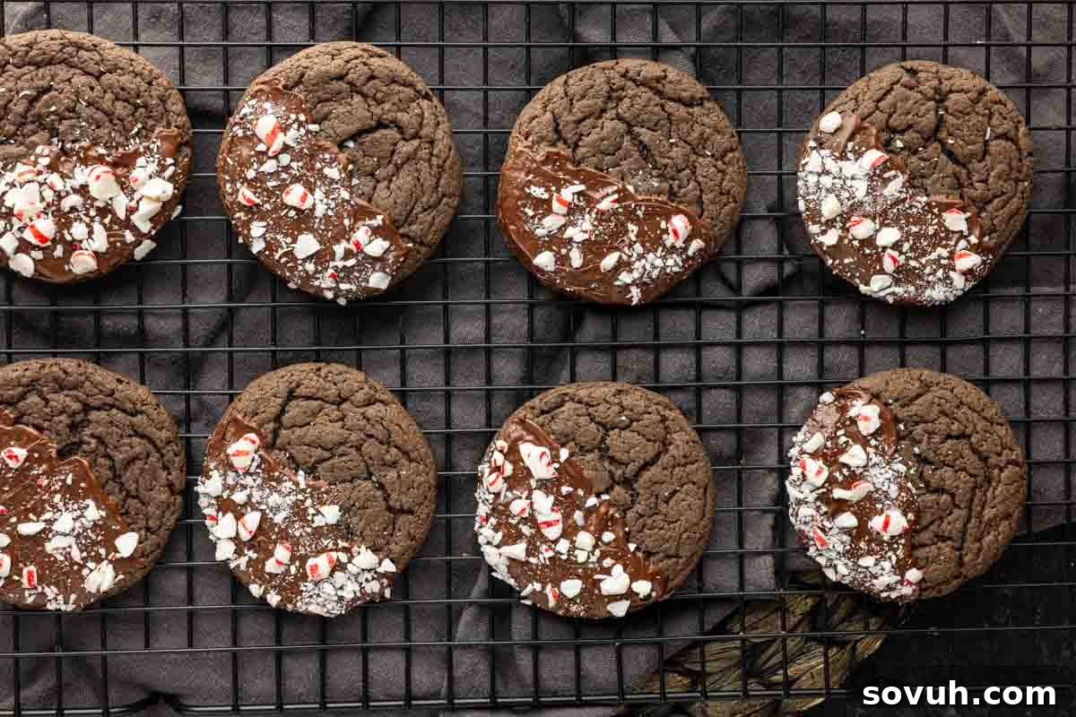 Eight easy peppermint cake mix cookies are partially dipped in chocolate and sprinkled with crushed peppermint, resting on a black wire cooling rack.