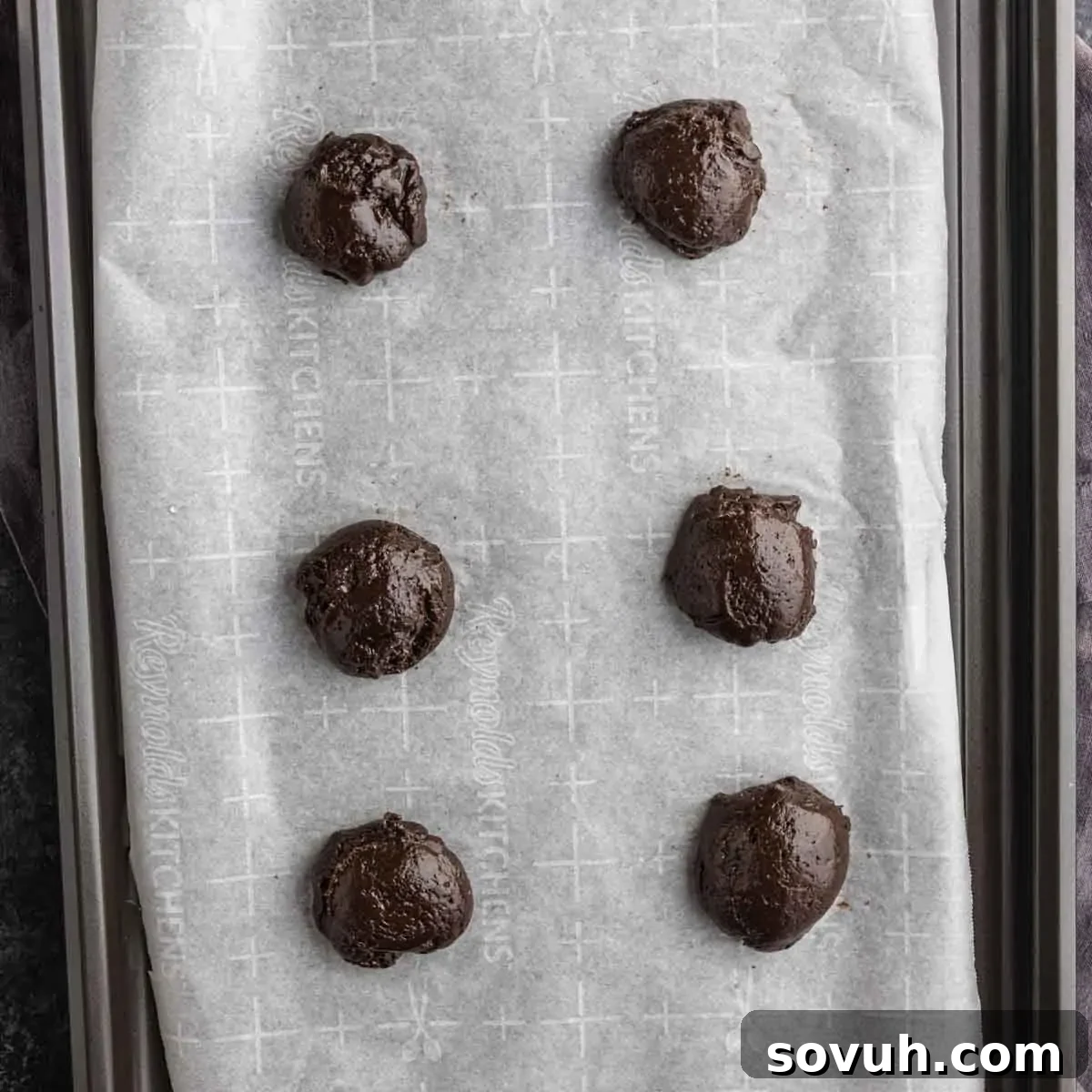Six scoops of chocolate peppermint cake mix cookies dough are placed on a parchment-lined baking sheet, spaced evenly apart in two columns.