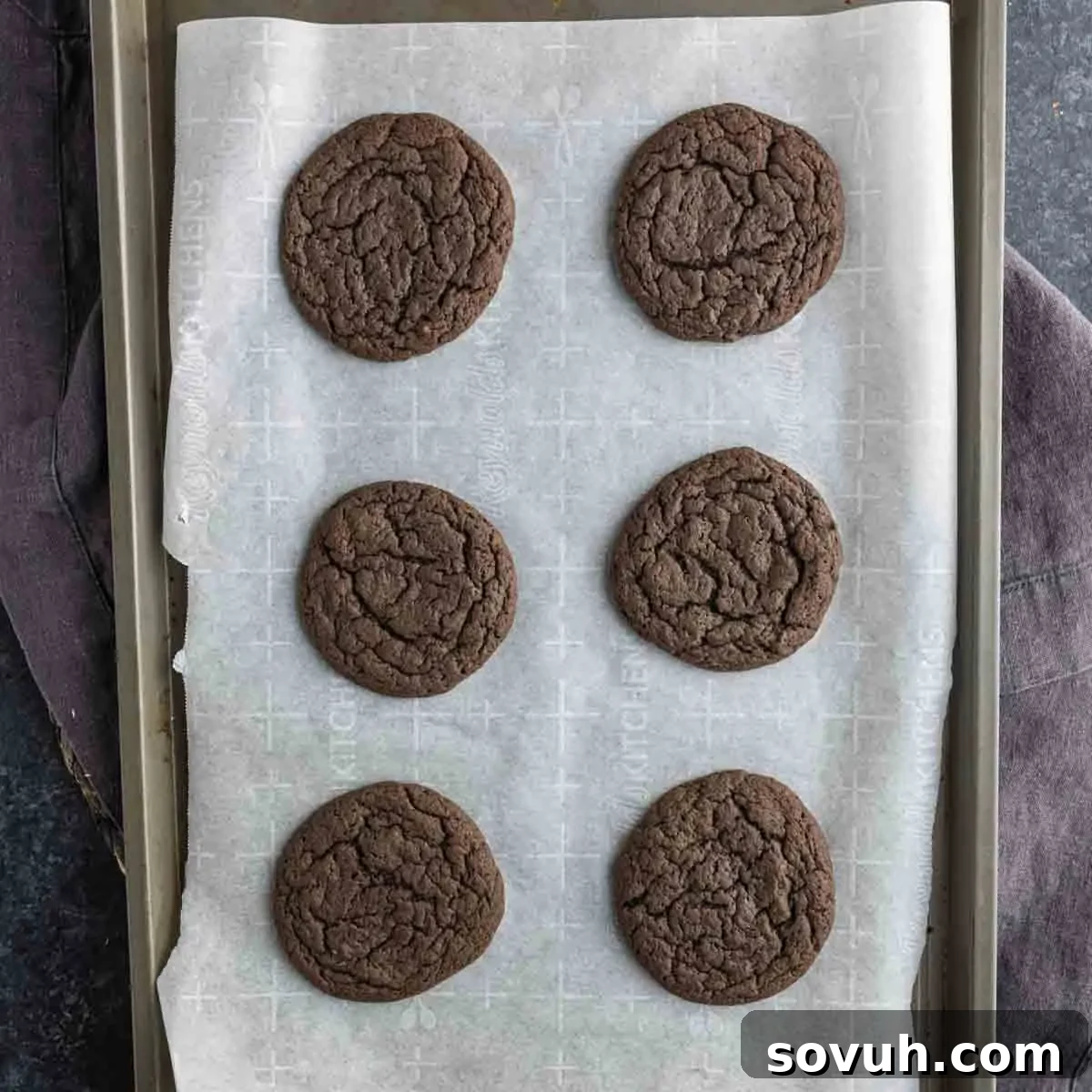 Six chocolate peppermint cake mix cookies are arranged in two columns on a parchment-lined baking sheet.
