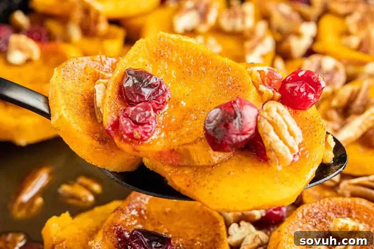Close-up of a spoonful of roasted sweet potato slices topped with cranberries and pecans, with more of the same in the background.