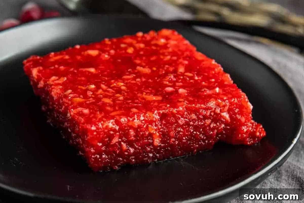 A square piece of bright red cranberry halwa with a slightly glossy texture, served on a black plate.