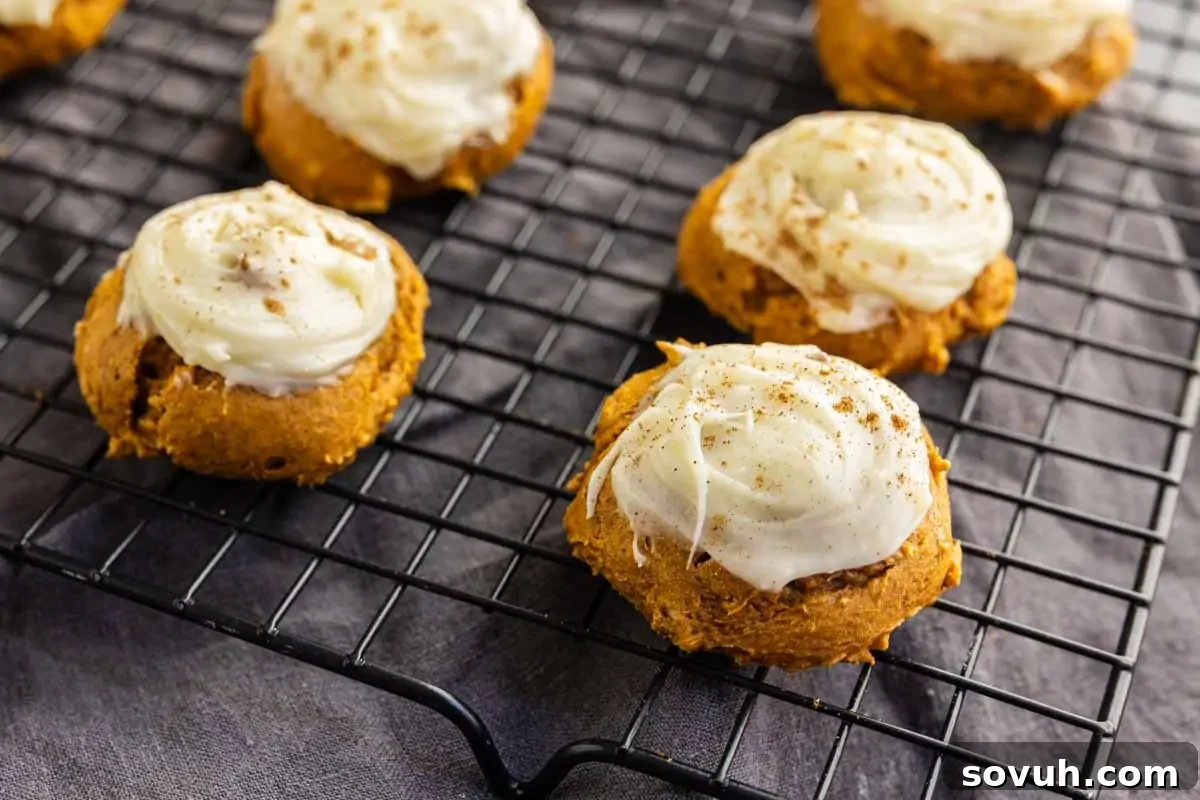 Pumpkin cookies with white icing and a dusting of spices are cooling on a black wire rack.