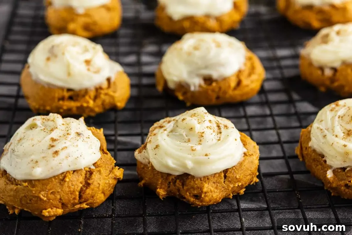 Pumpkin cookies topped with white frosting and a sprinkle of spice are arranged on a black cooling rack—perfect as easy Thanksgiving desserts for your holiday table.