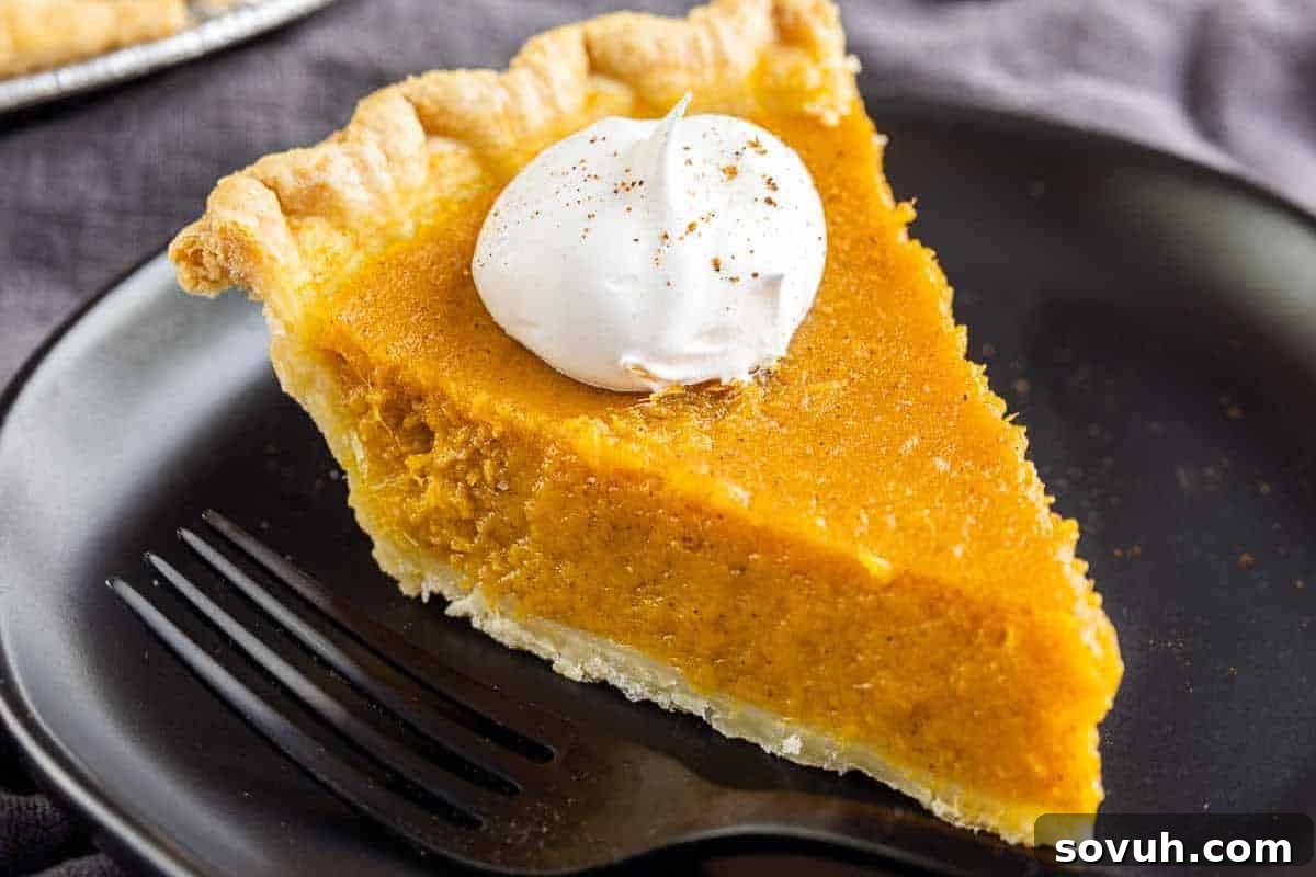A slice of pumpkin pie with a dollop of whipped cream on a black plate, accompanied by a black fork.