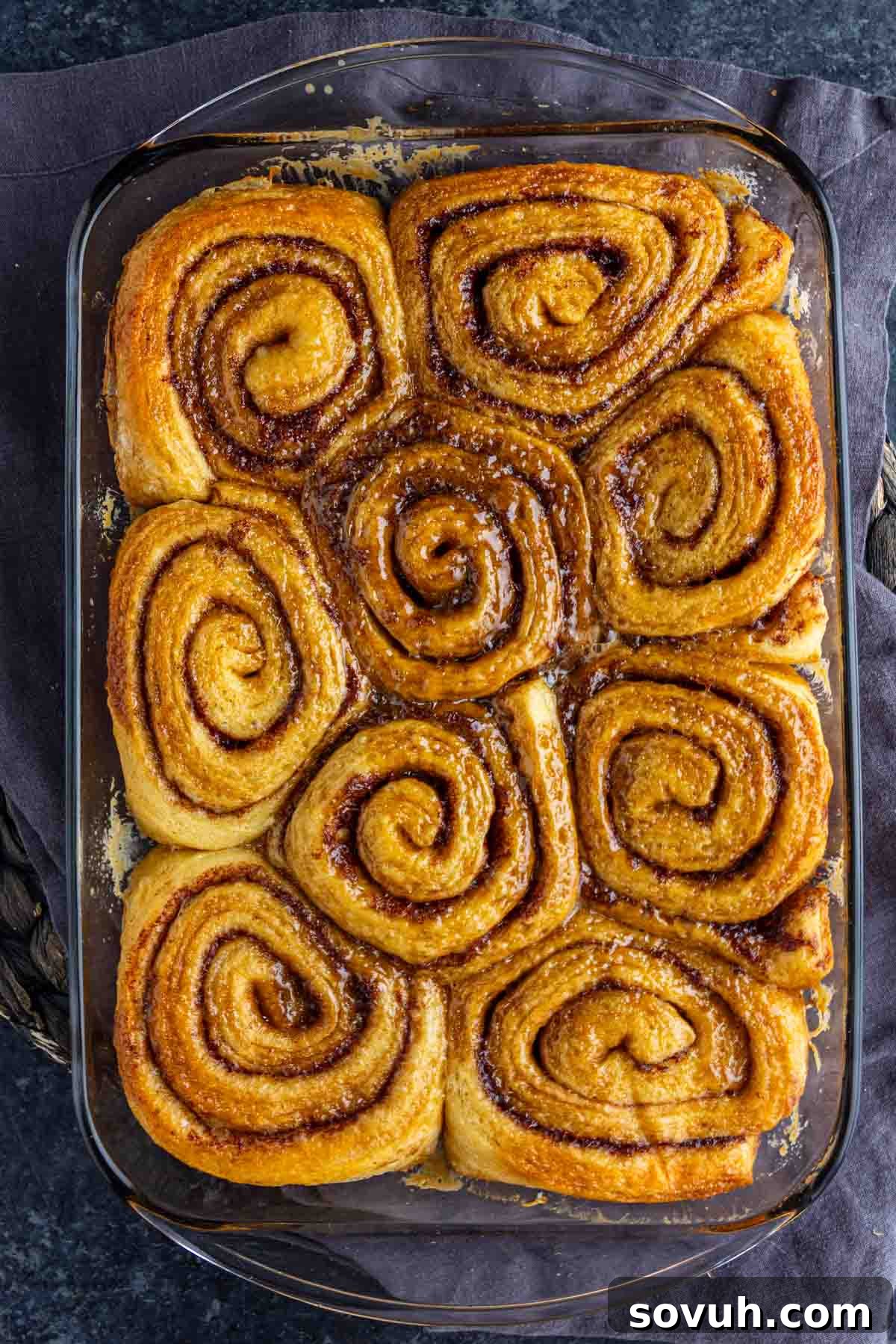 A glass baking dish filled with nine perfectly baked, glistening cinnamon rolls, arranged closely together, awaiting their frosting. This image captures the delicious outcome of the viral TikTok cinnamon roll hack, highlighting the golden-brown tops and promising soft, gooey interiors.