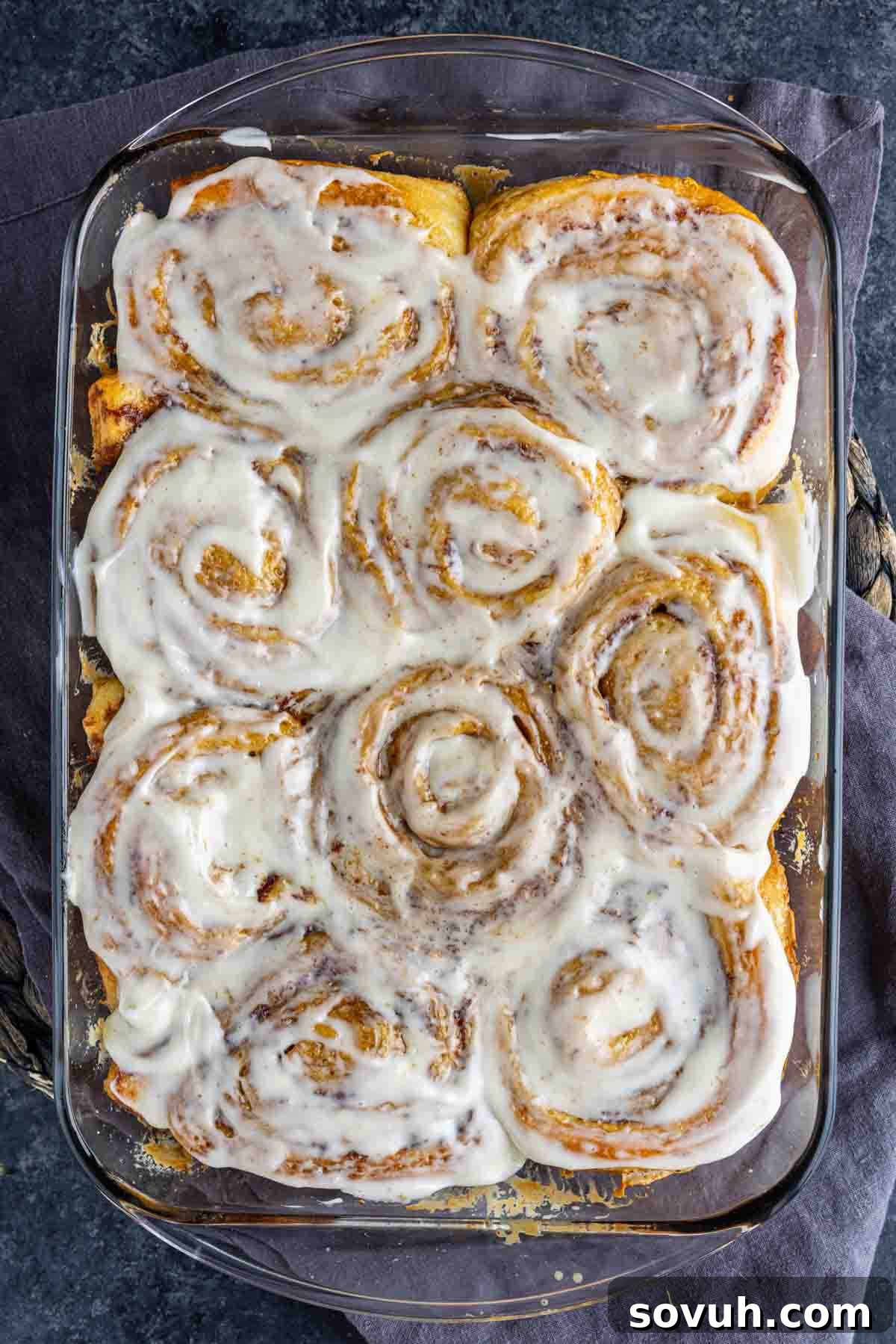 A full glass baking dish showcasing nine perfectly frosted TikTok cinnamon rolls with heavy cream, arranged closely together and covered with a generous, luscious layer of white icing. This image emphasizes the rich and inviting final presentation of the viral recipe.