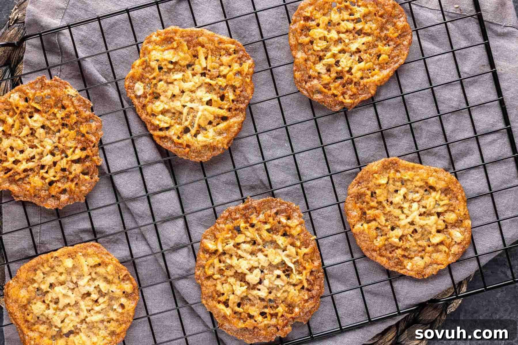 Six thin, golden brown lace cookies—Santa Approved—cooling on a wire rack placed over a gray cloth, perfect for your Christmas Cookies platter, showcasing their delicate texture.