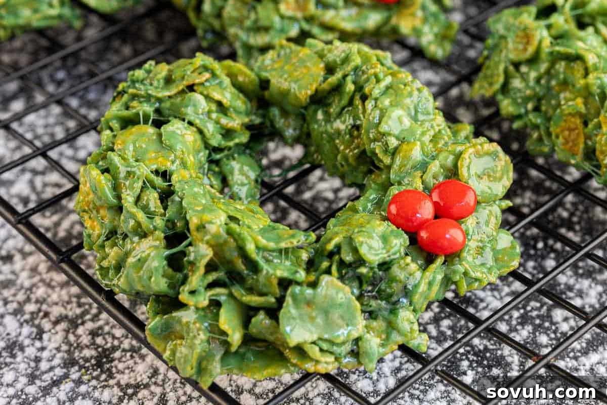 Green cornflake wreath cookies with festive red candy decorations on a cooling rack, embodying holiday cheer.