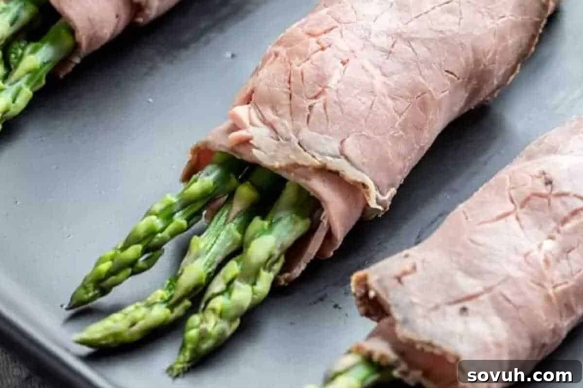 Asparagus spears wrapped in slices of roast beef on a dark surface.