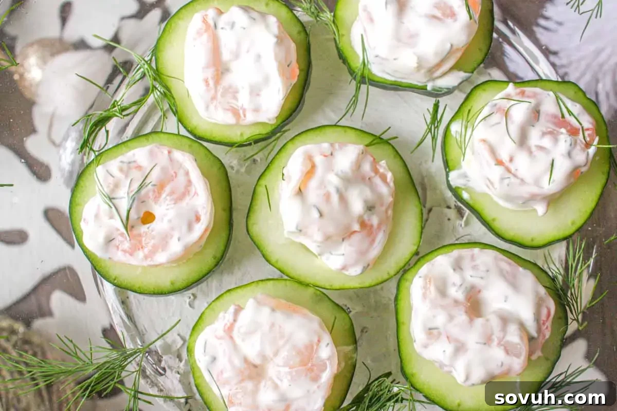 Cucumber slices topped with creamy shrimp salad, garnished with dill, arranged on a glass plate.