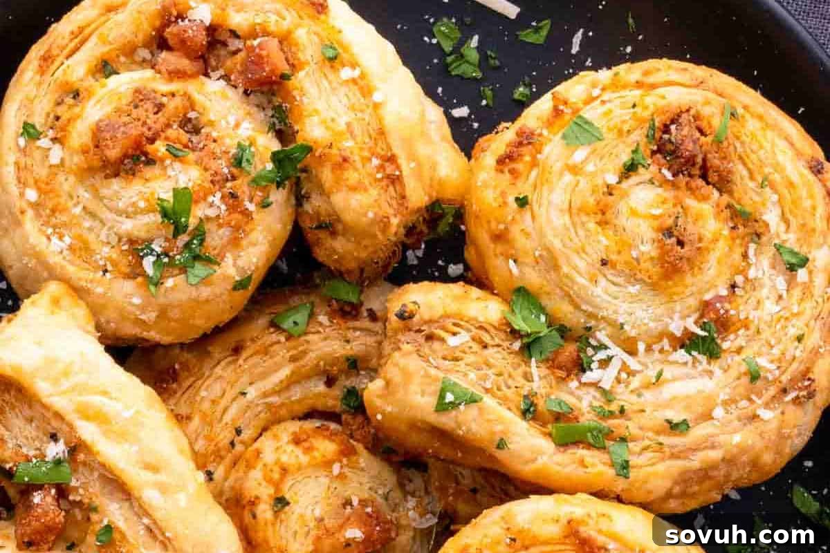 Close-up of baked spiral pastries garnished with chopped herbs and cheese, placed on a black plate.