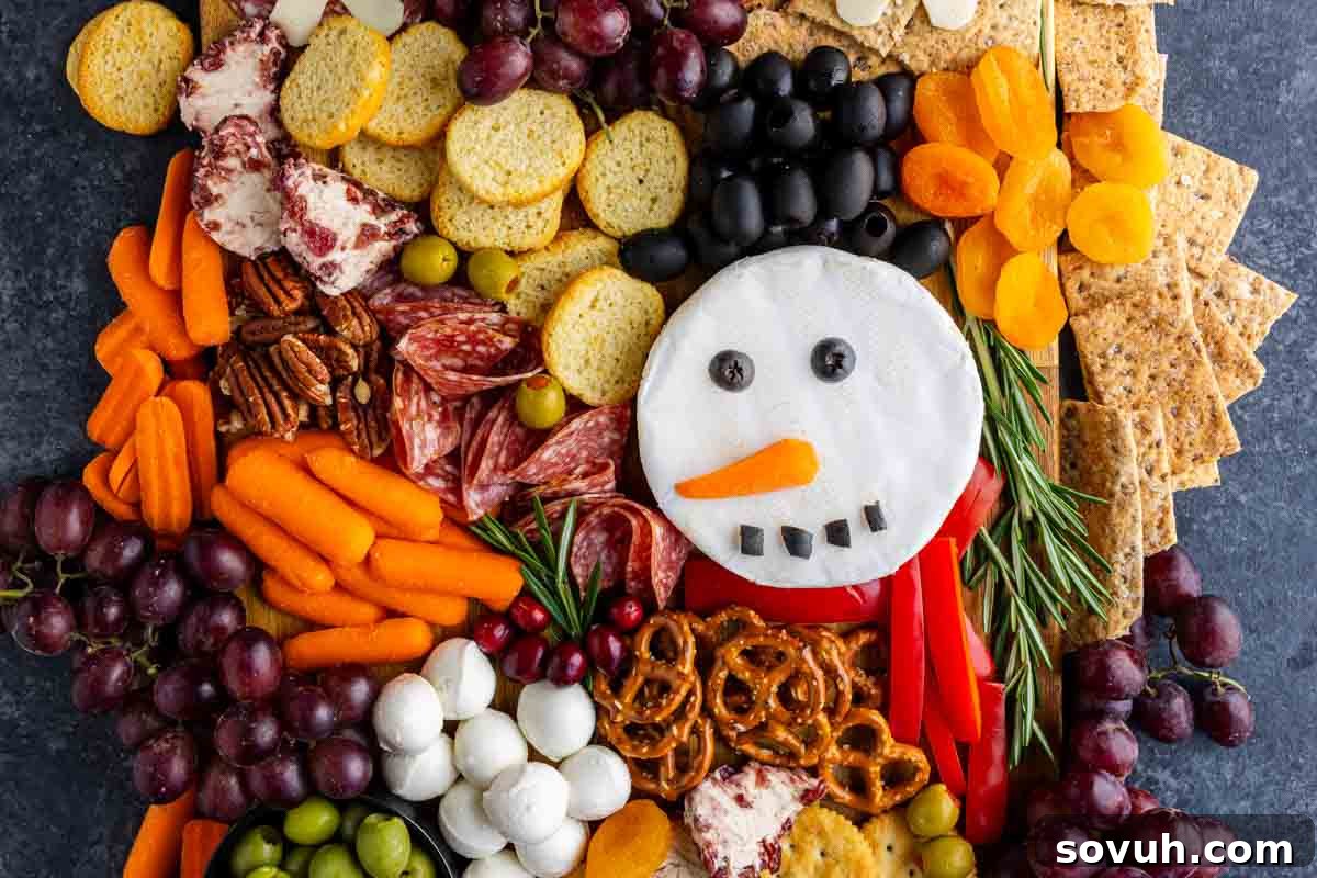 A festive charcuterie board with meats, cheeses, crackers, fruits, nuts, and veggies features a snowman face made from round cheese topped with olives and a carrot—perfect for your Christmas charcuterie board.