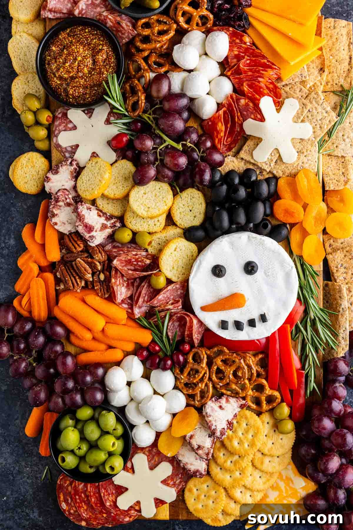 A festive charcuterie board with assorted crackers, cheeses, meats, fruits, veggies, and a snowman-shaped cheese decorated with olives, carrots, and peppers makes the perfect holiday charcuterie board for your Christmas gatherings.