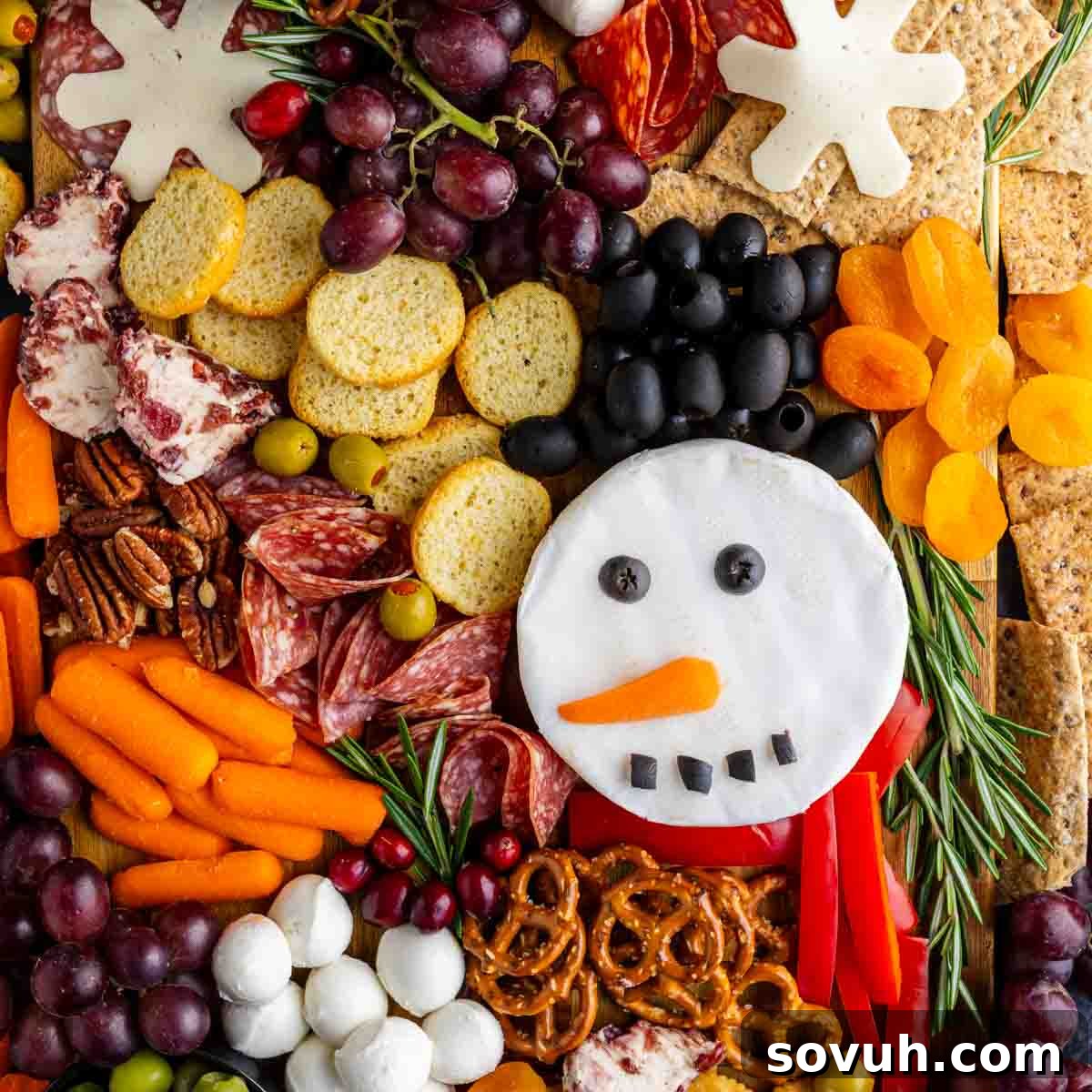 A Christmas charcuterie board perfect for easy holiday entertaining, featuring crackers, meats, cheese, fruits, nuts, pretzels, and veggies arranged as a snowman face with olive hair and a carrot nose.
