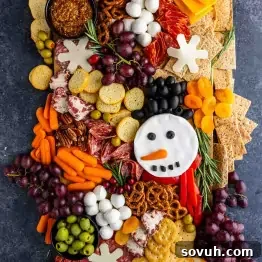A festive Christmas charcuterie board featuring assorted meats, cheeses, crackers, grapes, carrots, olives, pretzels, and a snowman-shaped cheese decorated with vegetables—perfect for easy holiday entertaining.