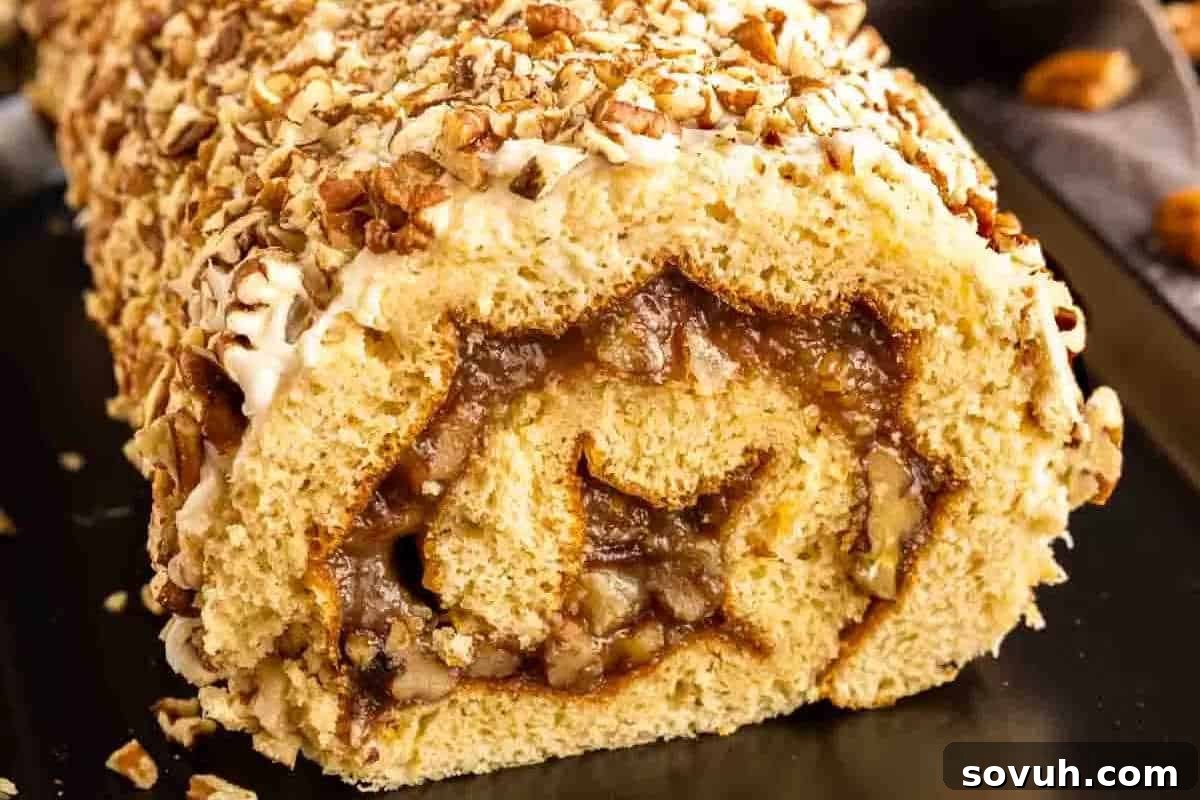 Close-up of a sliced roll cake filled with a caramel-like spread, topped with chopped nuts.