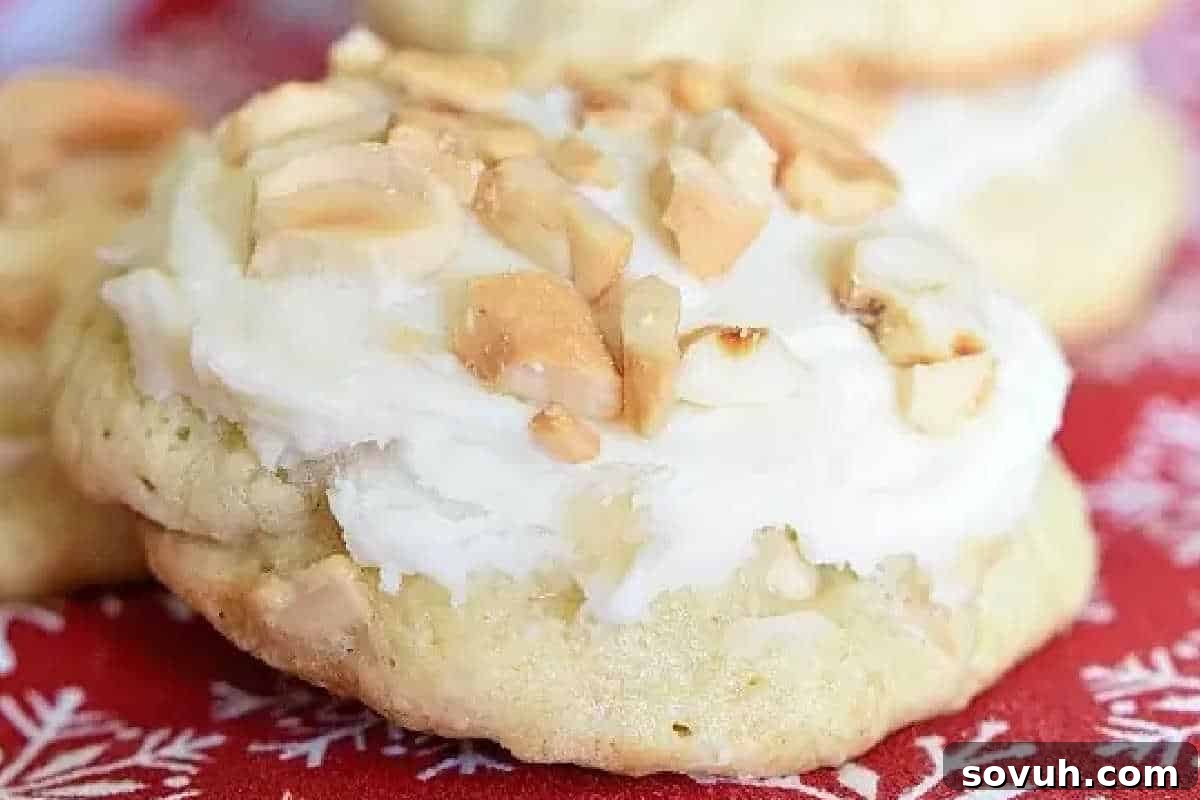 A close-up of a frosted cookie topped with chopped nuts, placed on a red cloth with a white snowflake pattern.