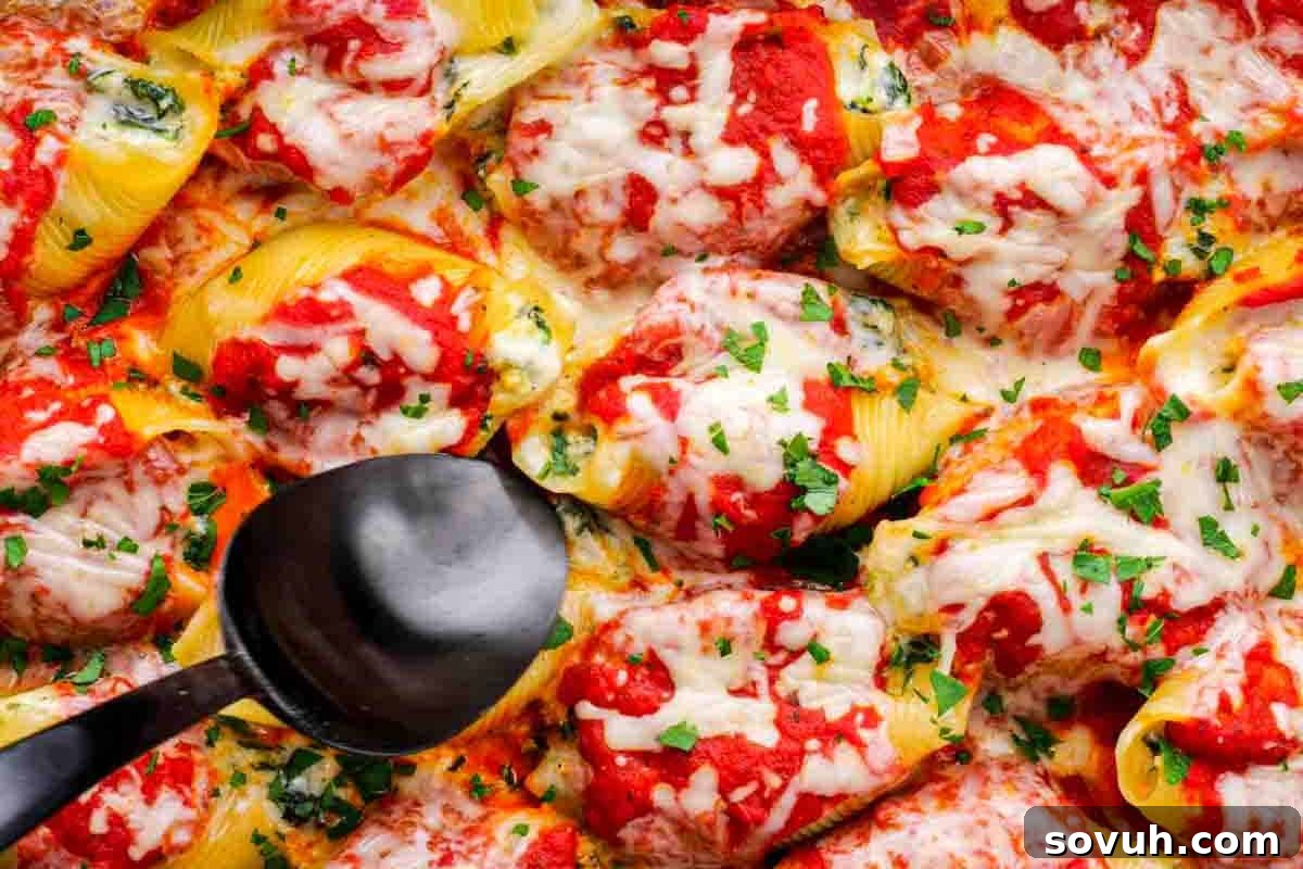 Stuffed pasta shells topped with tomato sauce, melted cheese, and chopped herbs, with a black serving spoon resting on the dish.