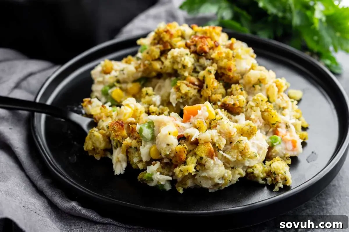 A serving of casserole with mixed vegetables and breadcrumbs on a black plate with a fork, garnished with herbs in the background.
