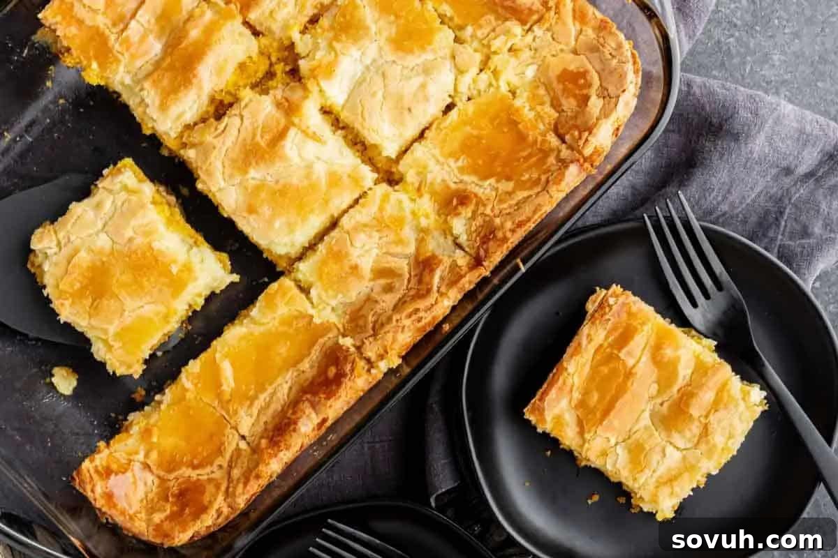 A glass baking dish with golden brown cake squares, one piece served on a black plate with a fork beside it.