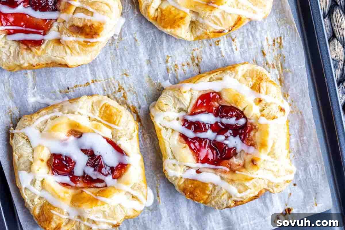 Close-up of cherry danishes with glaze drizzled on top, placed on a baking tray lined with parchment paper.