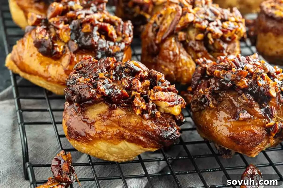 Close-up of sticky buns topped with caramelized pecans and glaze, cooling on a wire rack.