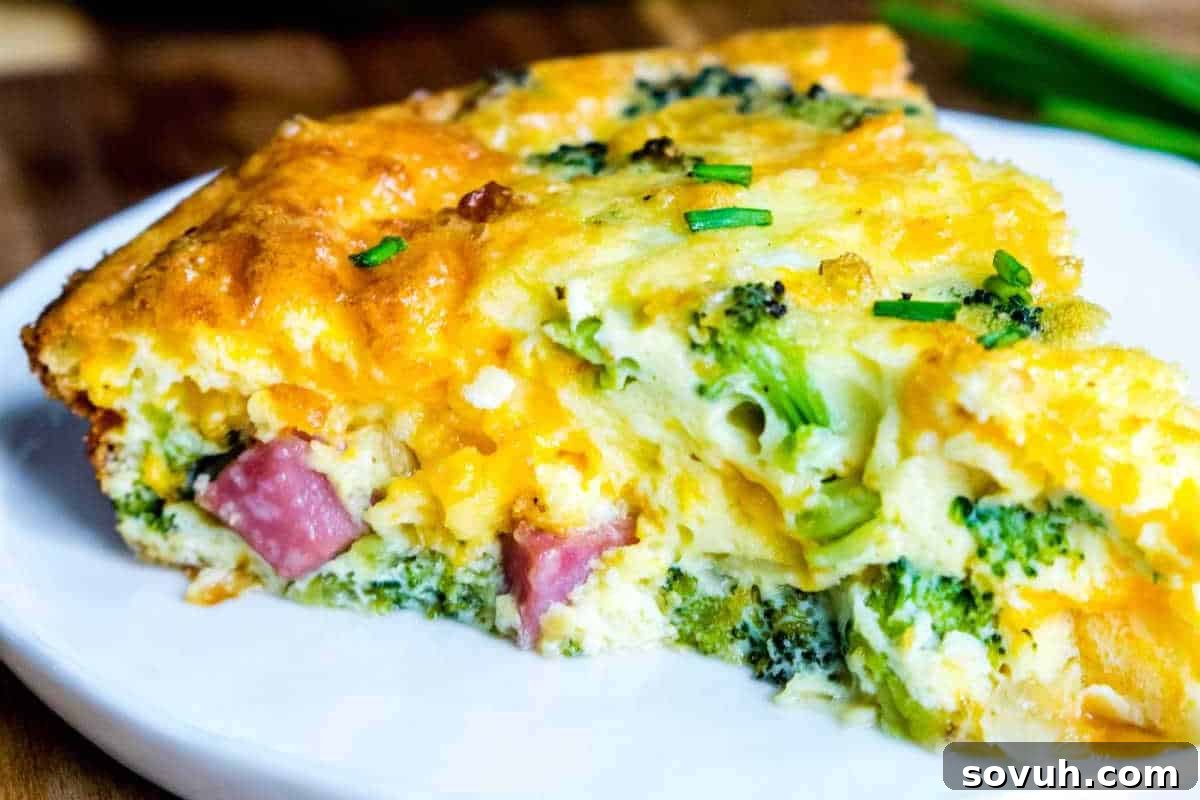 A slice of broccoli and ham quiche with a golden crust, served on a white plate.