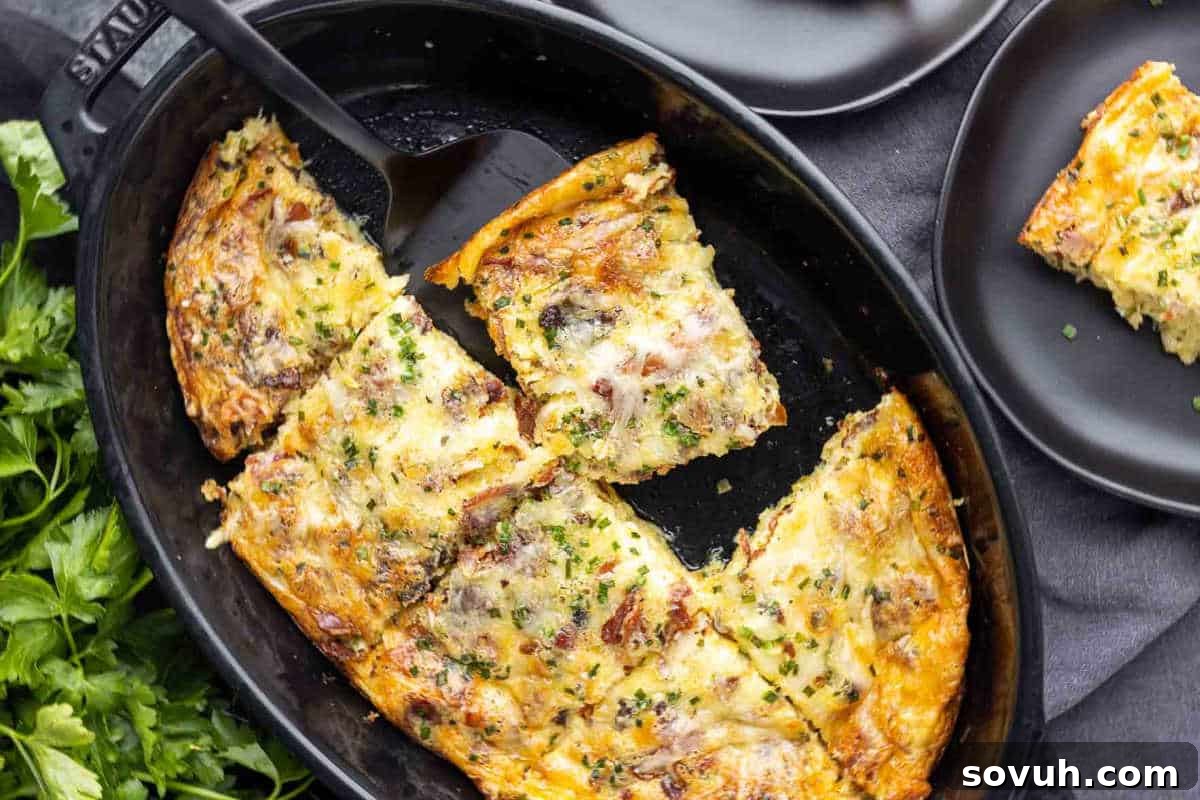 Baked casserole with cheese, herbs, and visible meat slices in a black oval dish, with a serving spatula.
