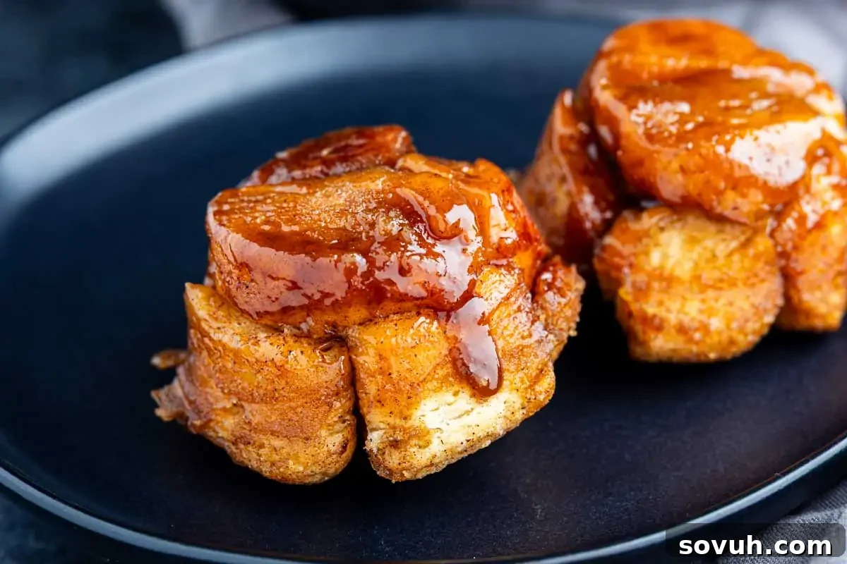 Two sticky, caramel-glazed monkey bread muffins are served on a black plate.